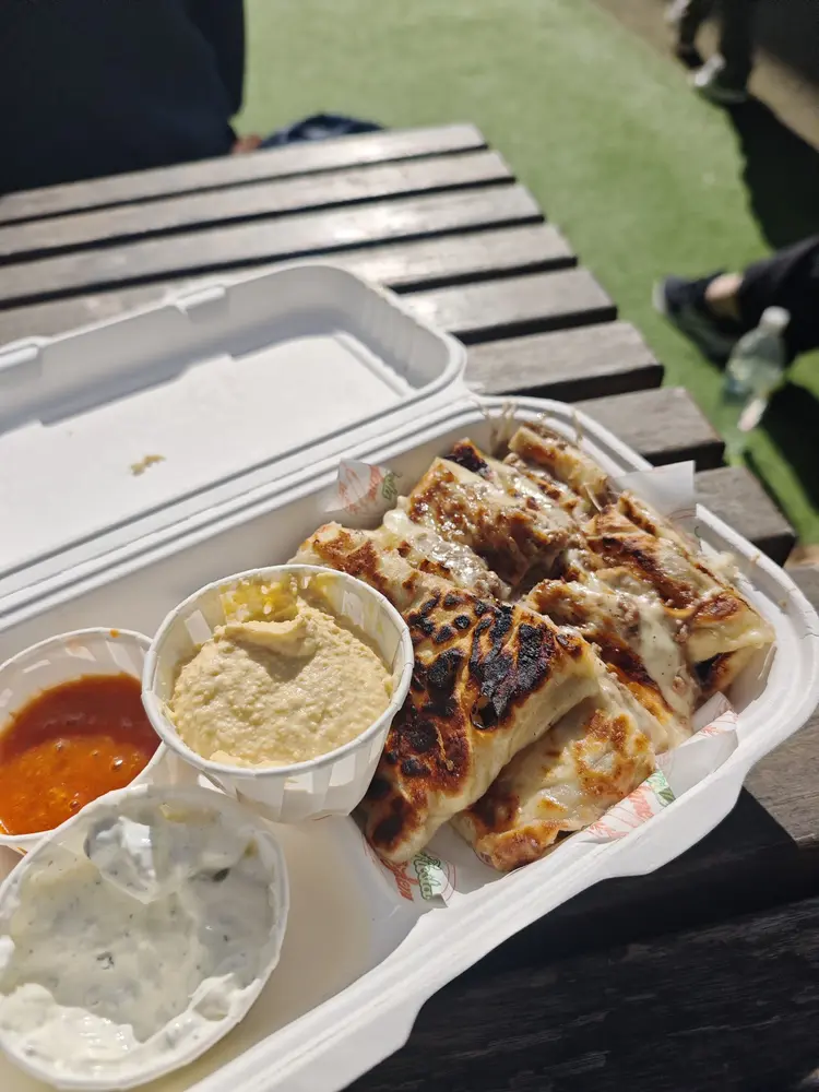 Beef and cheese gozleme in a box on a wooden table with hummus, garlic yoghurt and hot sauce