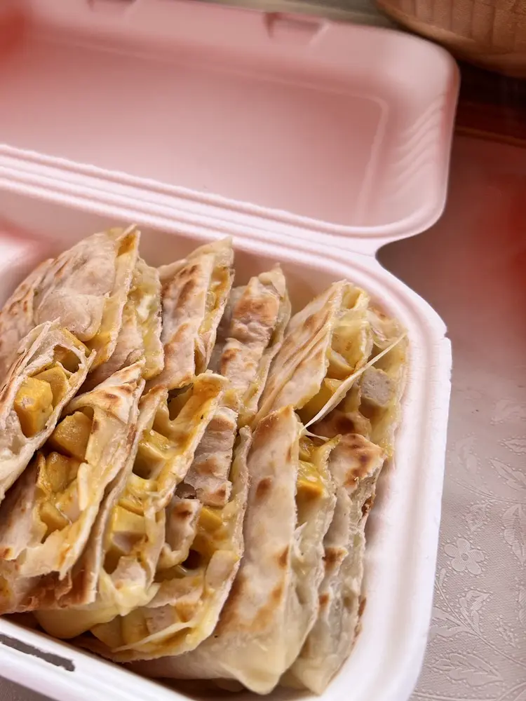 Sliced potato and cheese gozleme in a takeaway box beside pots of hummus and hot sauce