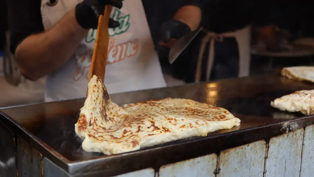 A cook lifting a gözleme off the hot griddle with a wooden spatula